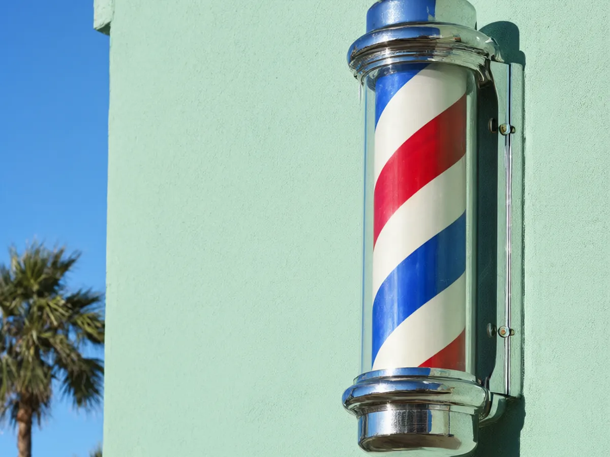 A red, white and blue barber pole on a mint-green storefront in the sun