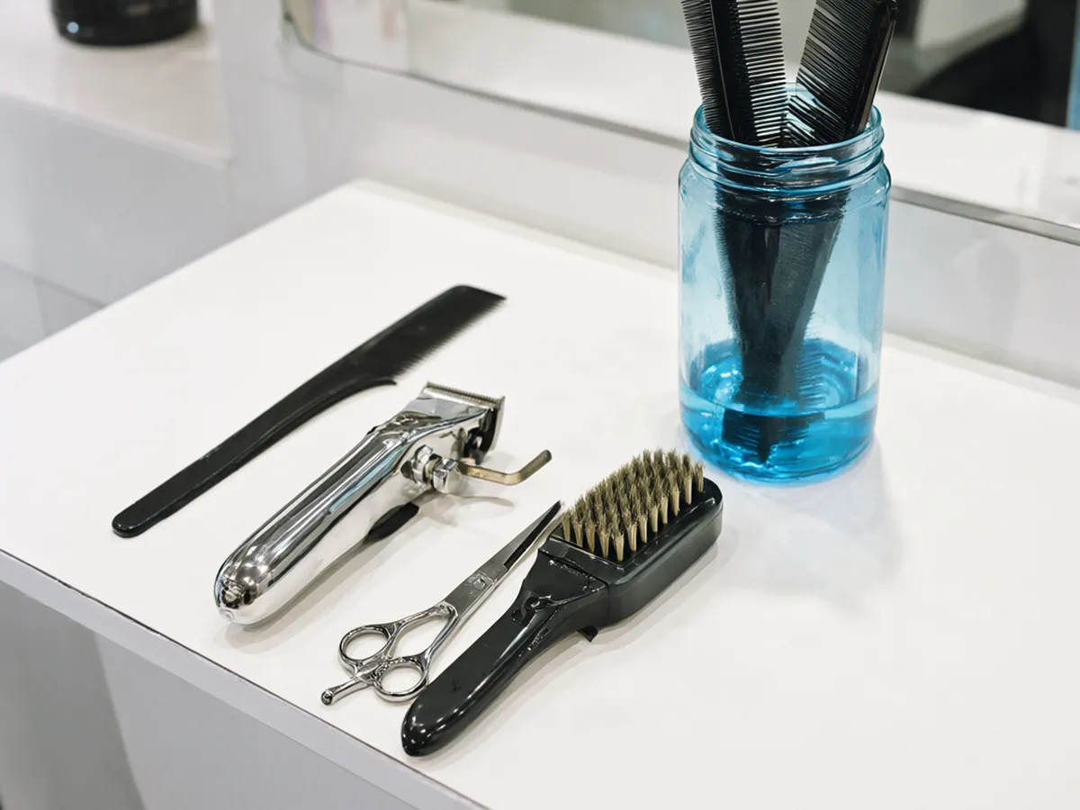 Combs, shears, a clipper and a neck brush beside a jar of blue disinfectant